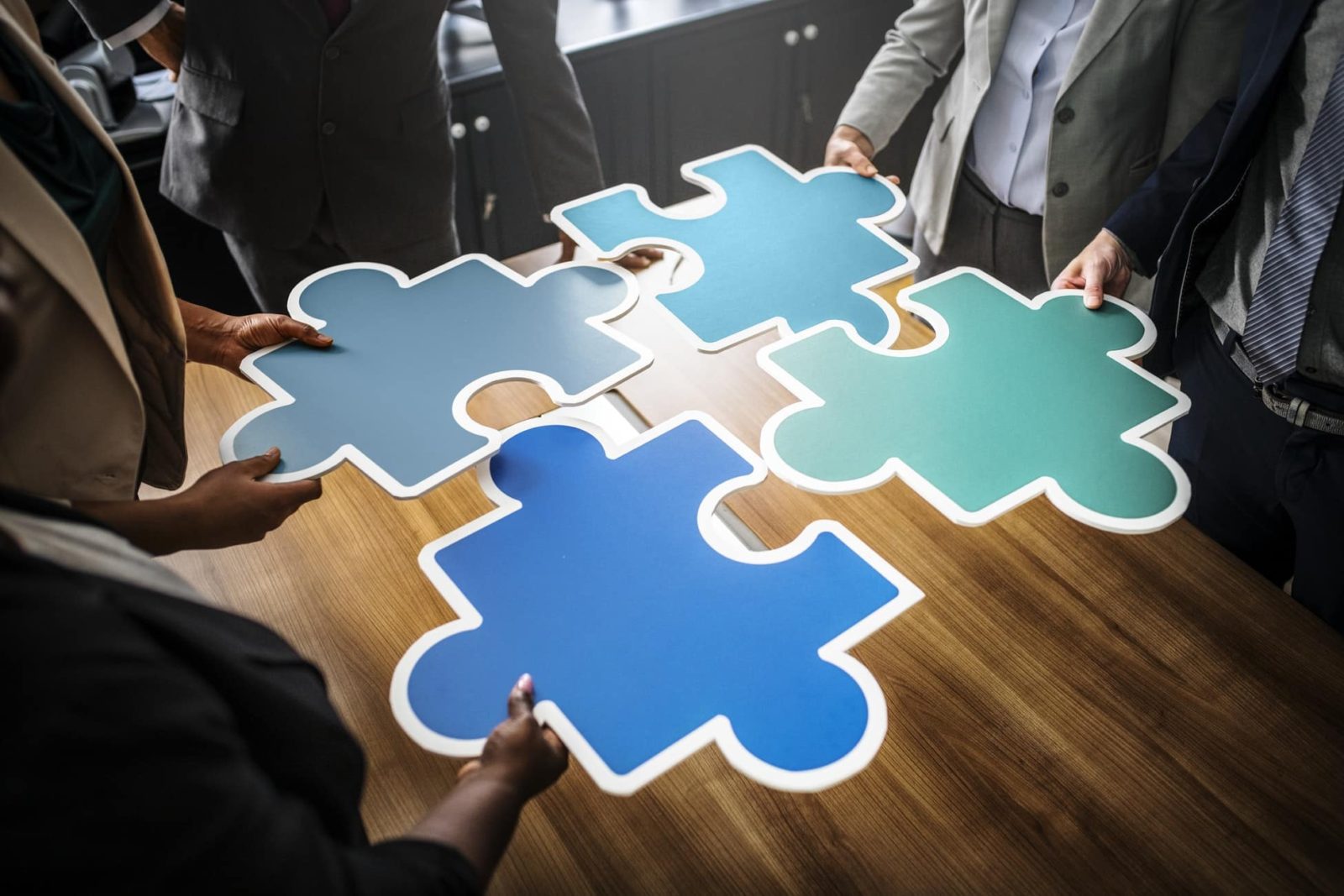 people hold four pieces of Puzzles to form a team work idea on a table
